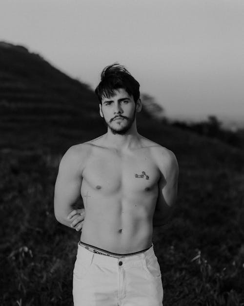 Shirtless Man in White Pants Standing at a Hill Slope