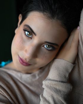 A close-up portrait of a woman with striking makeup resting her head on her hand.