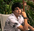 一位穿着棕榈树衬衫的时尚年轻人若有所思地坐在户外，抬起了头