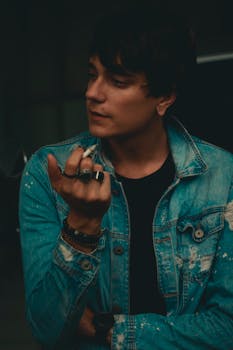 一个穿着牛仔夹克的时尚男人，手里夹着香烟，若有所思