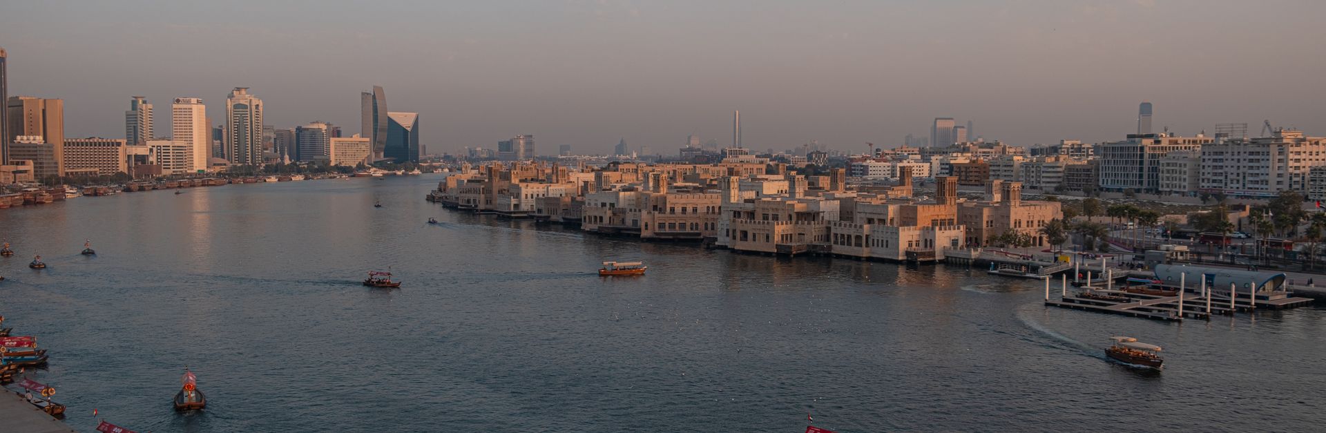 Panoramic view of Dubai Creek's waterfront and skyline at sunset.
