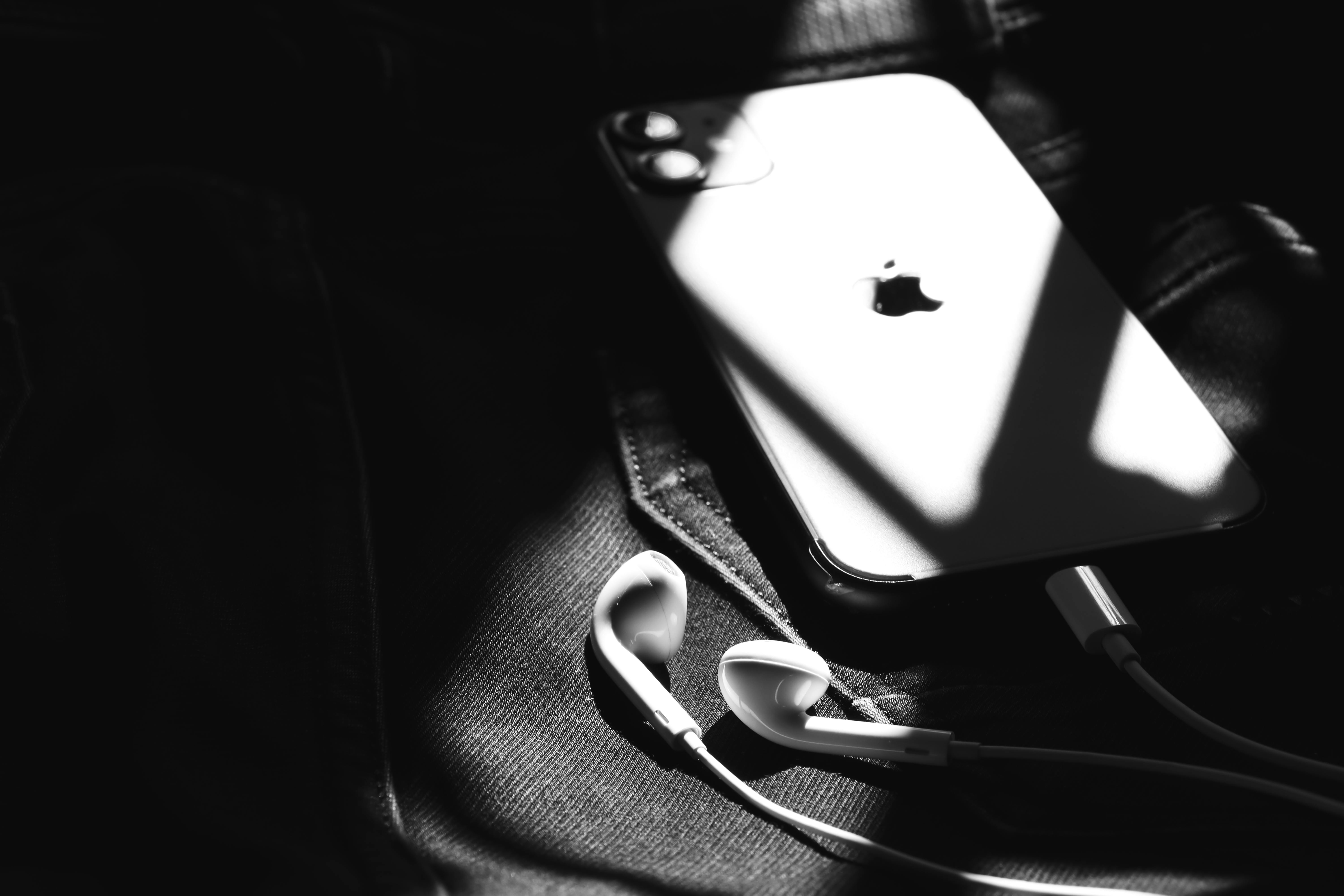 Black and white image of a smartphone with earphones on denim, captured in Patna, India.