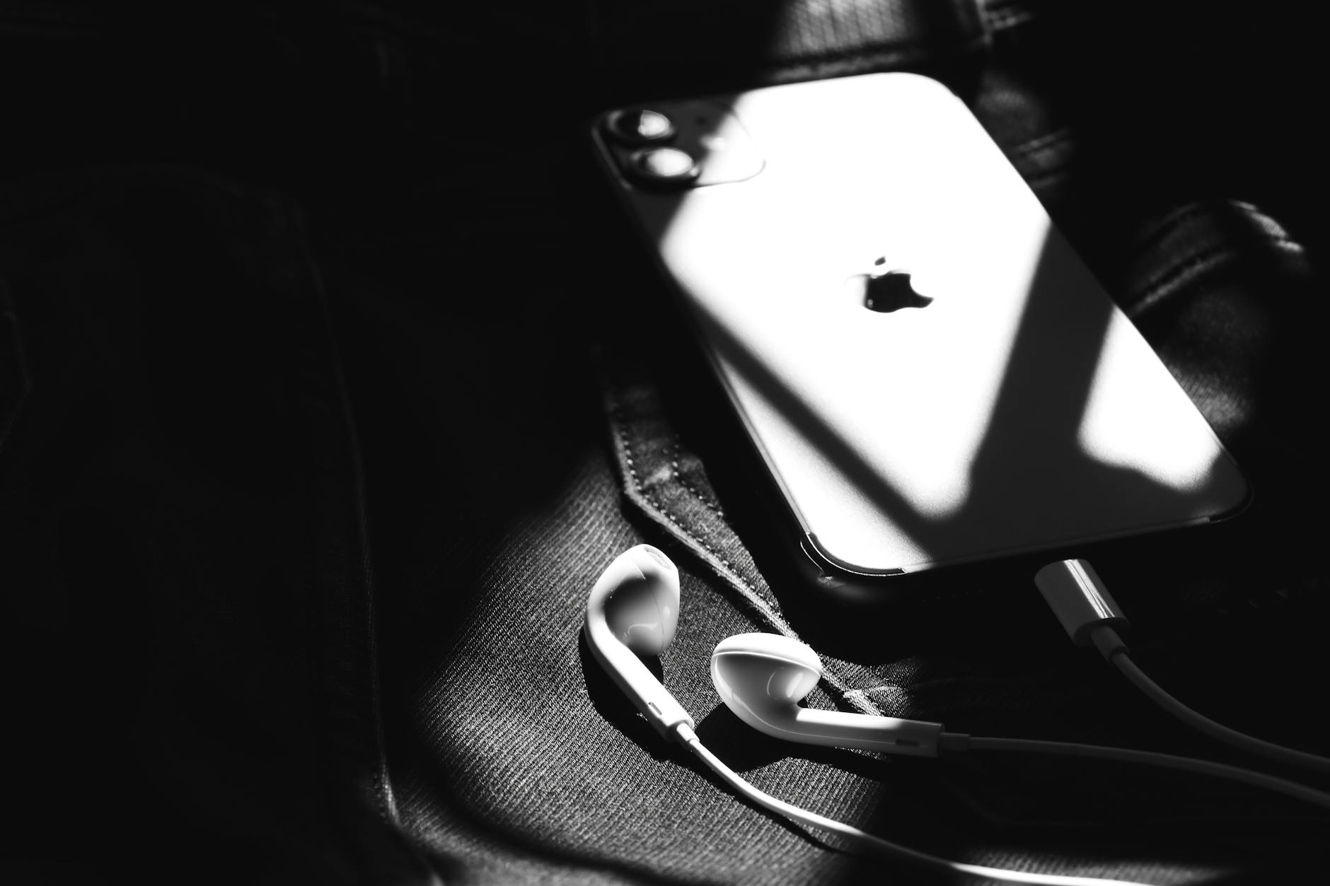 Black and white image of a smartphone with earphones on denim, captured in Patna, India.