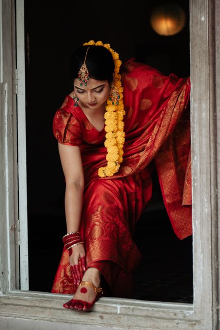 A woman in a vibrant red sari with floral decorations leaning out of a window, embracing rich cultural heritage.