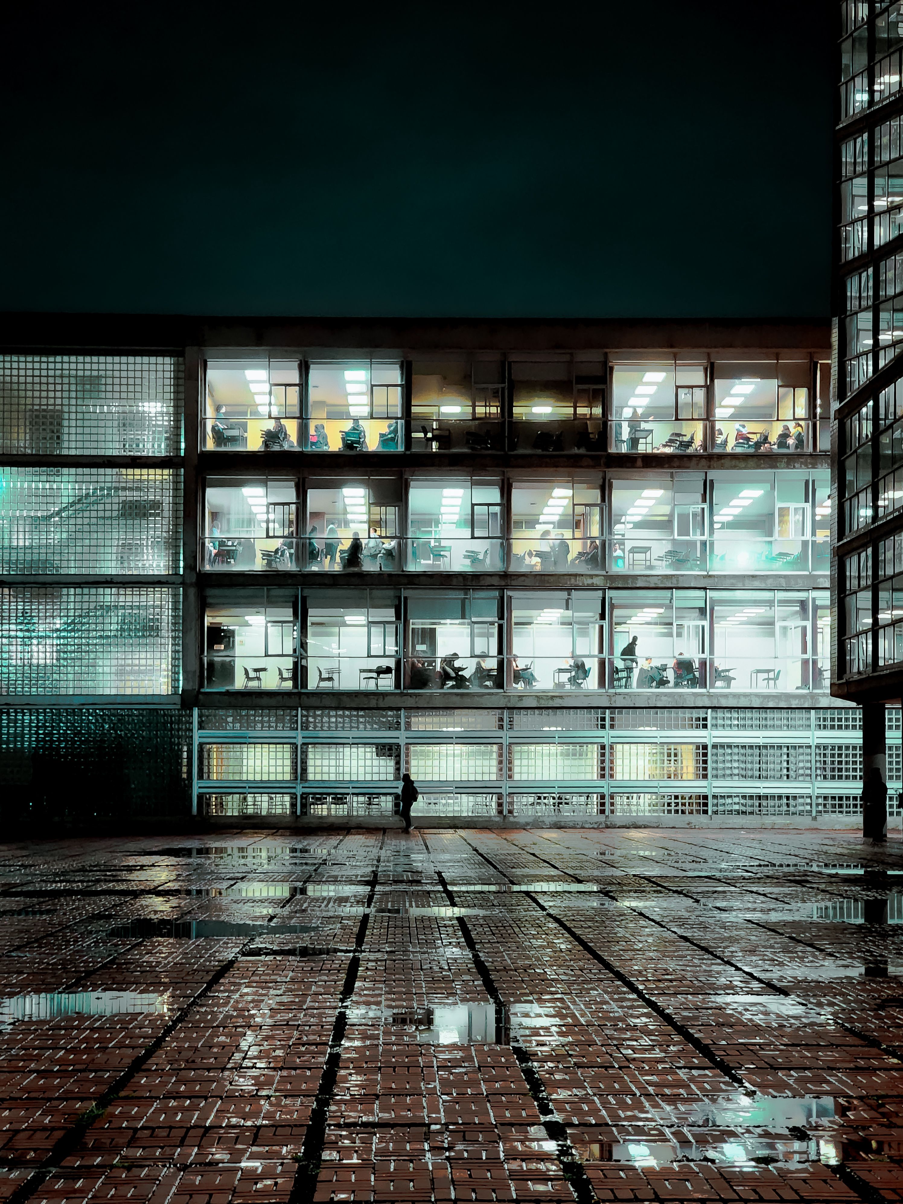Fotomural Edificio de oficinas con ventanas iluminadas en Ciudad de México por la noche en medio del pavimento mojado.
