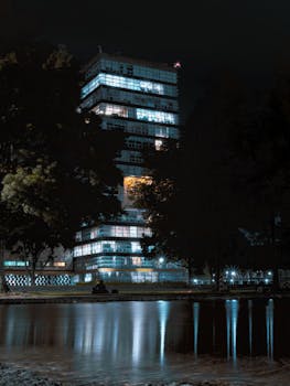 Modern high-rise building with glowing windows reflected in a pond at night in Mexico City.