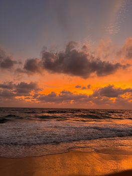 Stunning view of the ocean at sunset with a dramatic sky reflecting warm hues on the waves and sand.