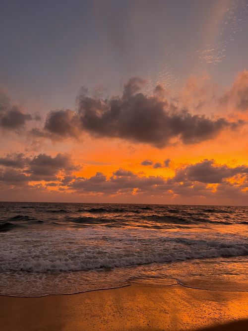 Free Stunning view of the ocean at sunset with a dramatic sky reflecting warm hues on the waves and sand. Stock Photo