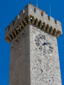 A vertical shot of the historic Mangana Tower in Cuenca, Spain, set against a clear blue sky.