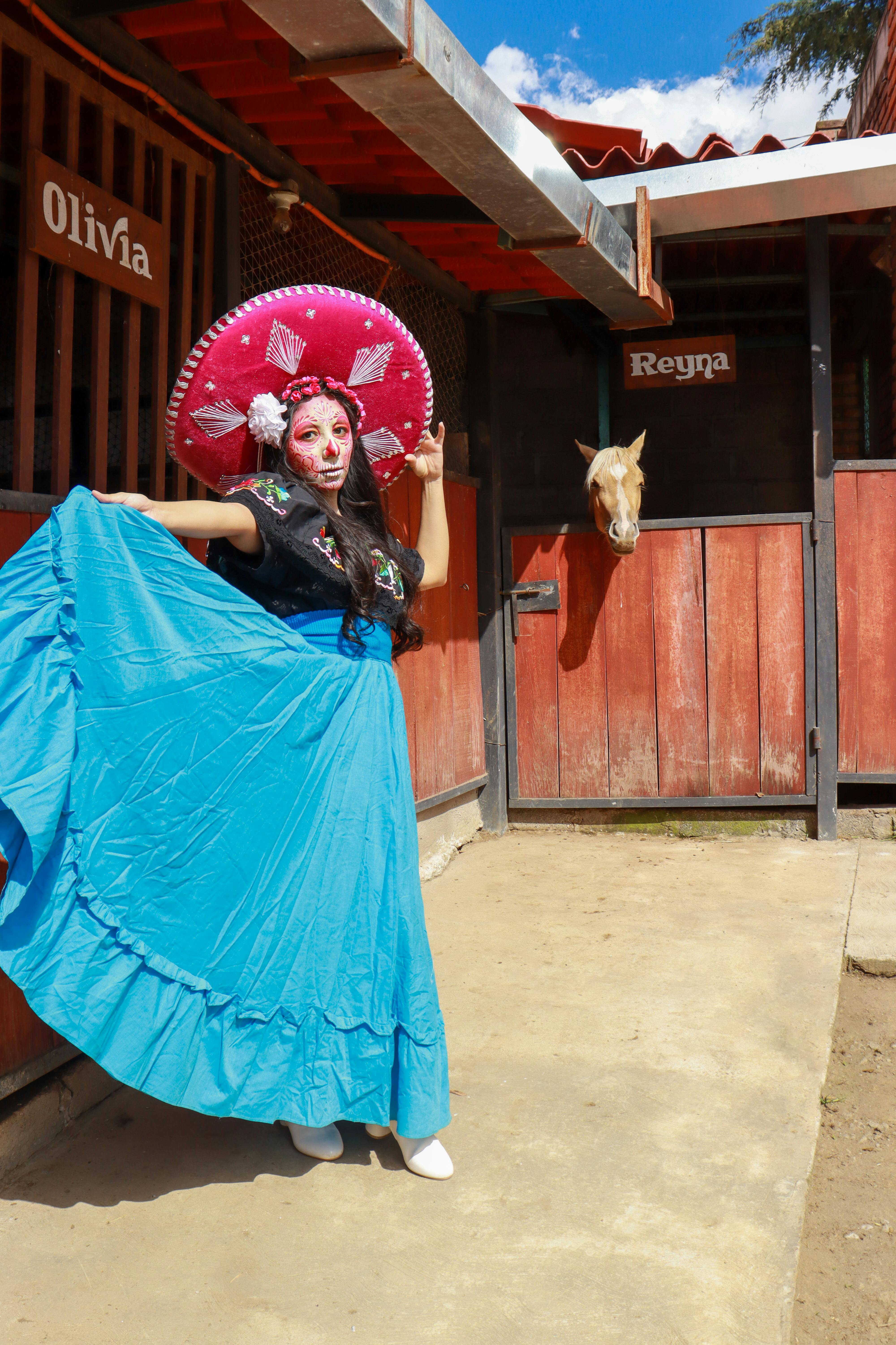 A woman in traditional Mexican attire poses near a stable in vibrant cultural celebration.