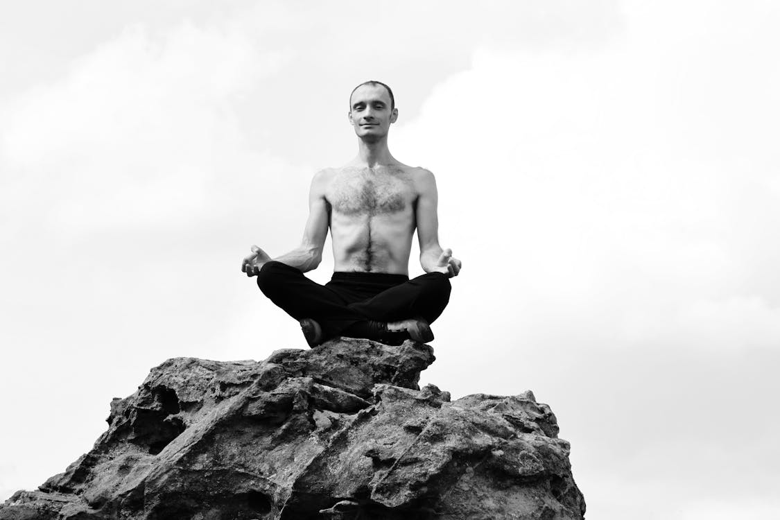 Free Man Meditating Shirtless on the Top of a Rock Stock Photo