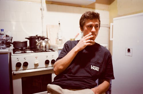 Young Man Sitting in the Kitchen and Smoking a Cigarette