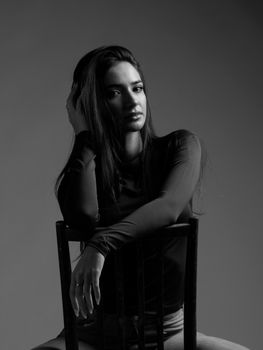 Captivating black and white portrait of a young woman sitting on a chair in a studio setting.