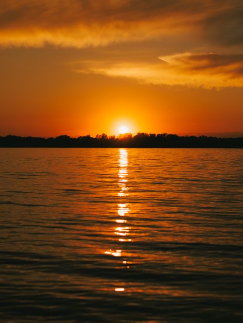 Free Captivating sunset casting a golden glow over tranquil lake waters, perfect for mobile wallpaper. Stock Photo