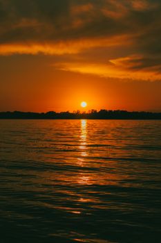 Breathtaking sunset view over a peaceful lake with a dramatic sky and silhouette trees.
