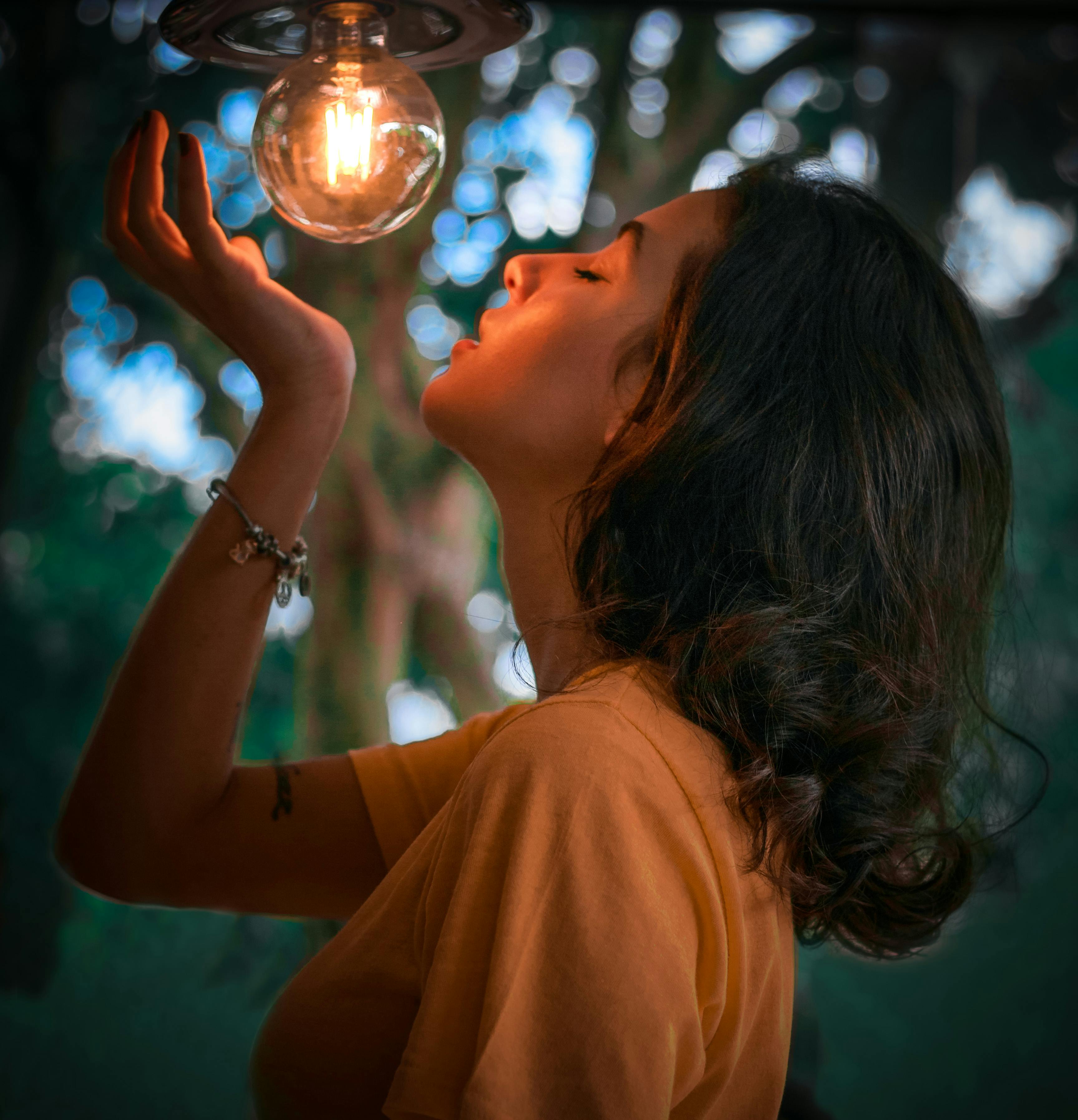 一位女士手持发光的灯泡，在宁静的户外环境中摆出姿势，营造出温暖而艺术的氛围