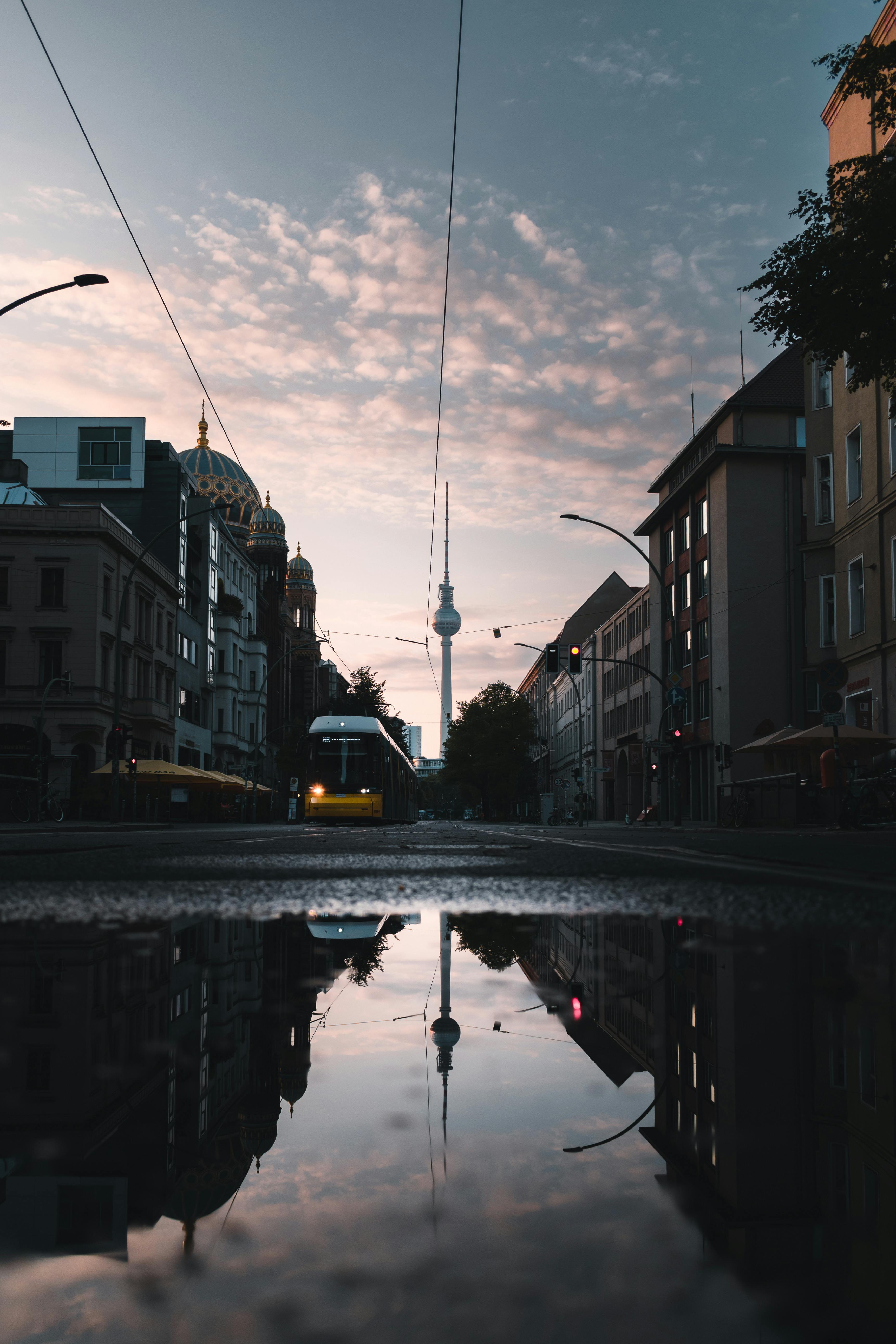 Urban scene in Berlin featuring the Fernsehturm reflected in a puddle with city architecture and tram.