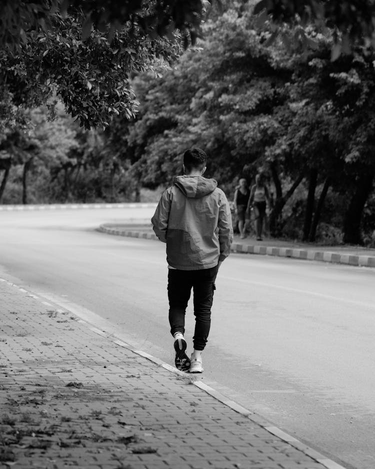 Grayscale Shot Of A Man Walking Down A Sidewalk