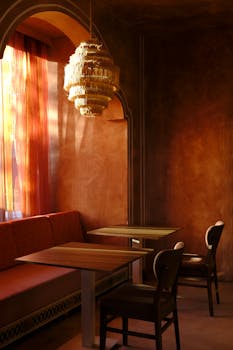 Sunlit cafe interior featuring wooden tables, chairs, and a unique chandelier against warm-toned walls.