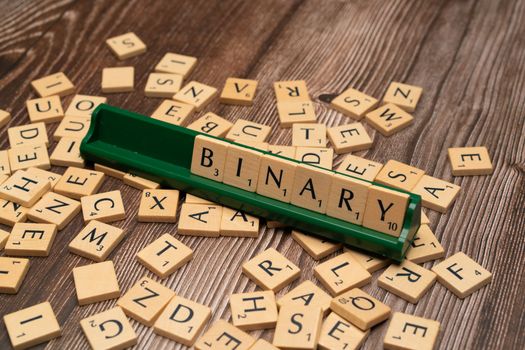 Close-up of scrabble tiles spelling 'Binary' surrounded by scattered letters on a wooden background.