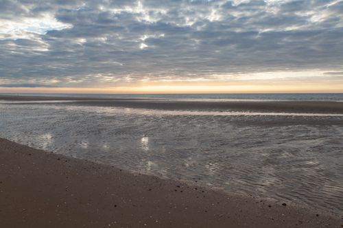 Free Scenic sunrise view over the beach in Cabourg, Normandy, with calm sea and cloudy skies. Stock Photo
