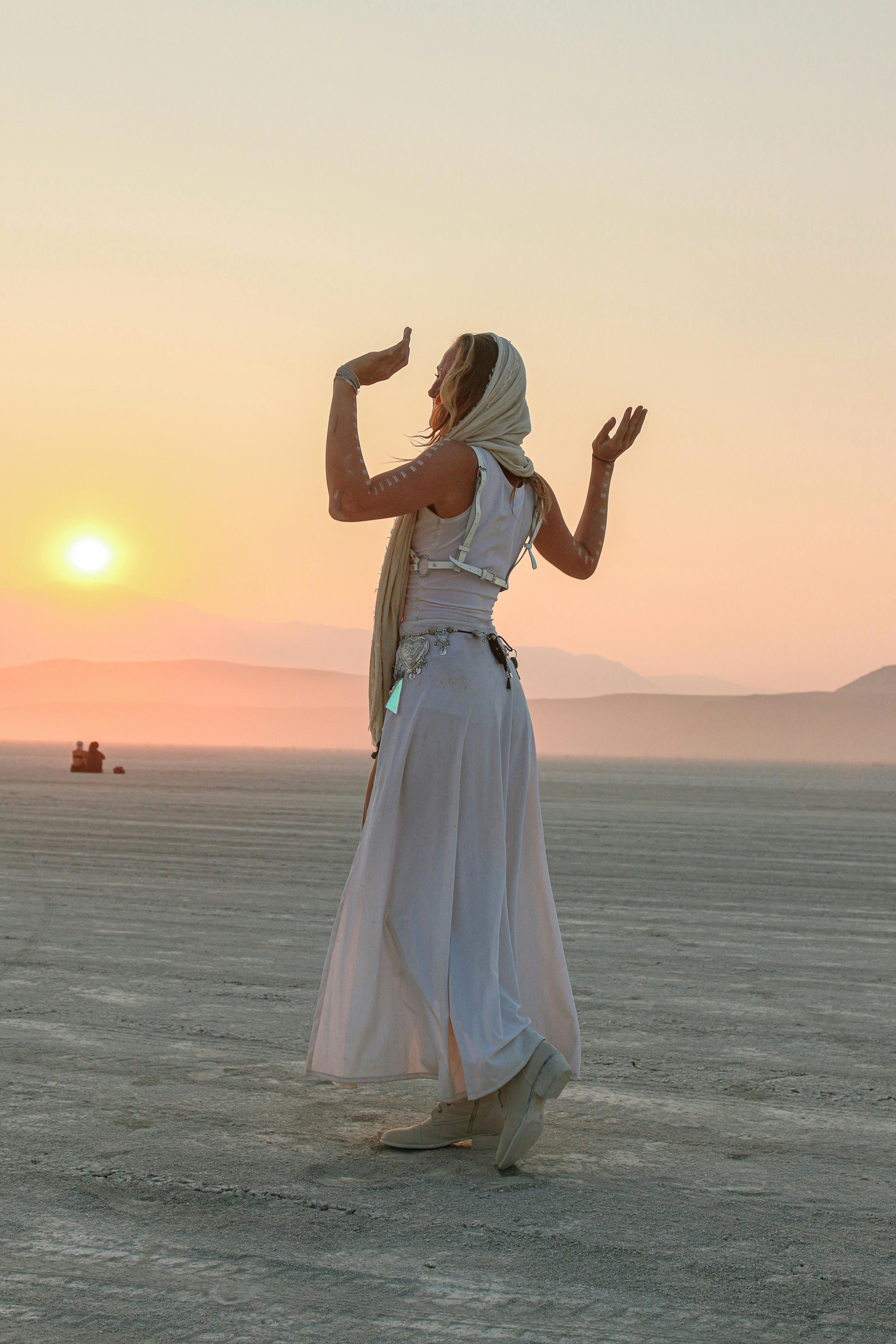 A woman dances gracefully in the desert during a serene sunset, creating a captivating silhouette.