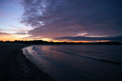 Free Captivating view of a sunset over a serene beach with gentle waves under a dramatic sky. Stock Photo