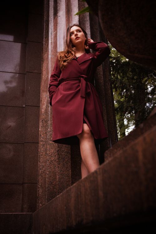 Free Stylish woman in red coat leans against urban wall exuding elegance and confidence. Stock Photo