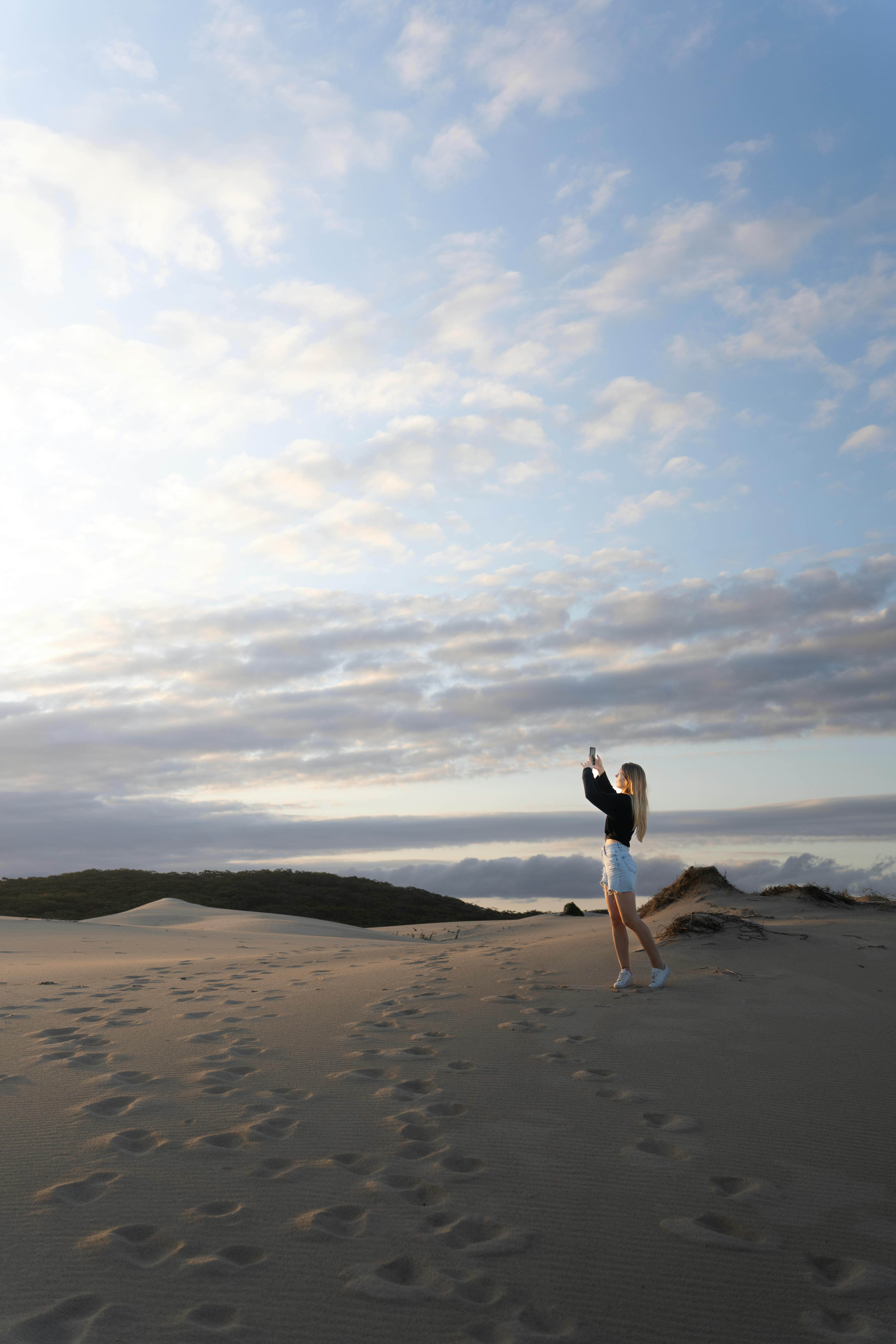 A woman photographs a serene beach landscape with her smartphone during the day.