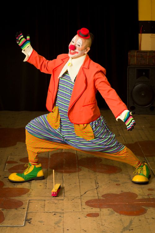 Free Cheerful clown in vibrant attire performing a playful act with a toy car on stage. Stock Photo