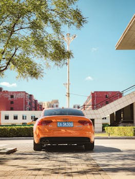 Orange Audi A5 sports car parked in a modern cityscape environment with clear blue skies.