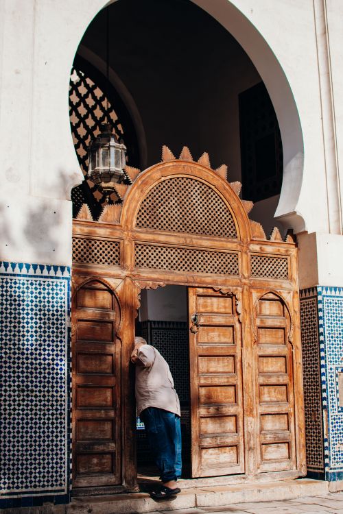 Free A man peeks inside a large wooden door of a mosque in Fez, Morocco, showcasing traditional Islamic architecture. Stock Photo