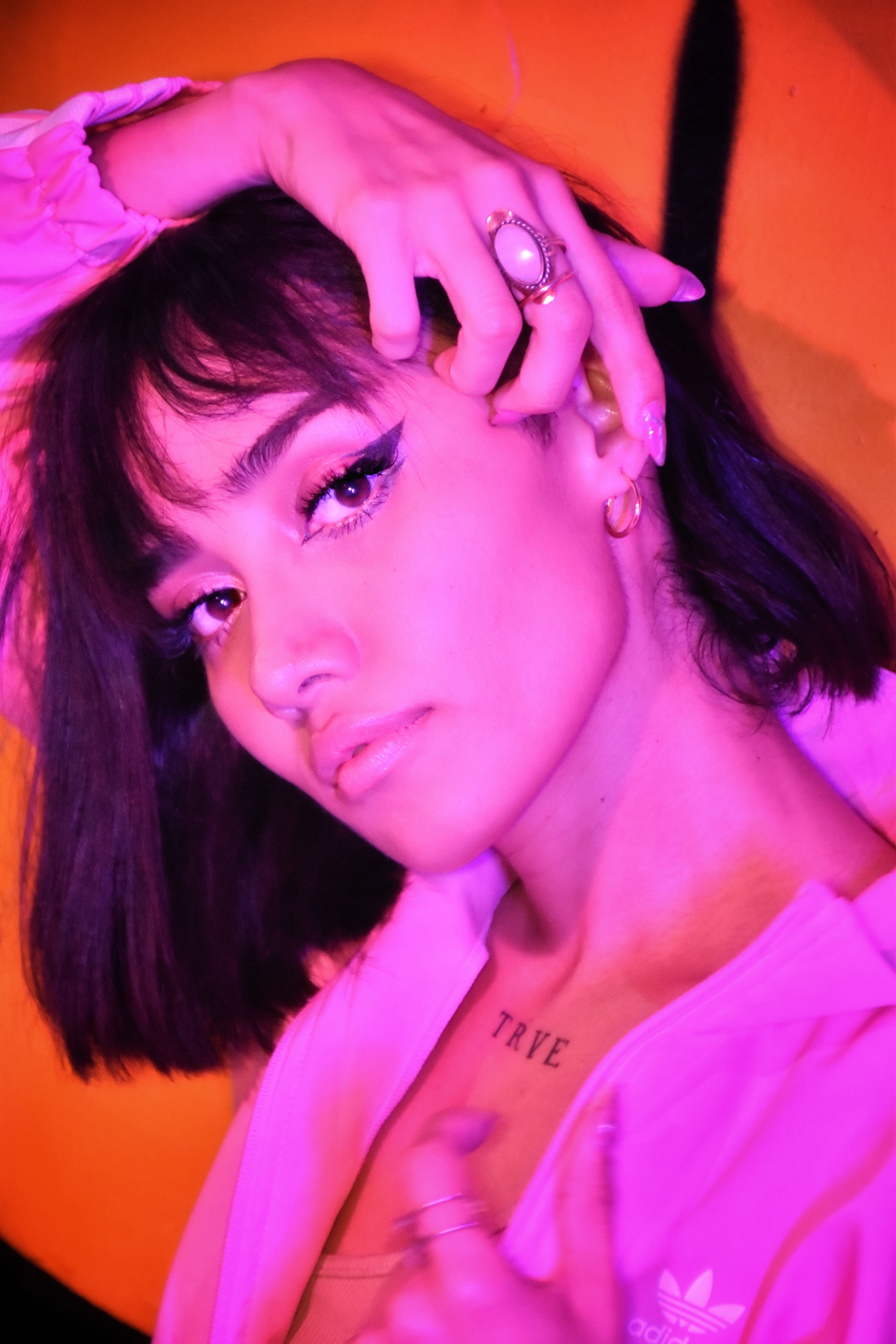 Artistic portrait of a woman with bold makeup and pink lighting.