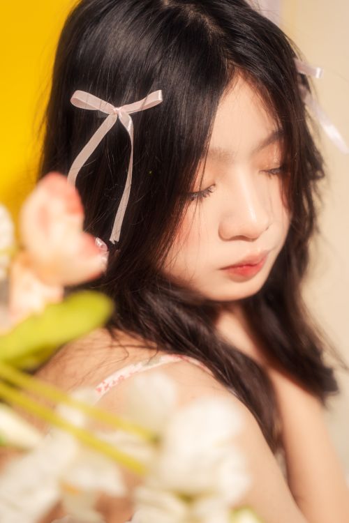 Free A serene close-up portrait of a young woman with closed eyes, wearing ribbons in her hair. Stock Photo