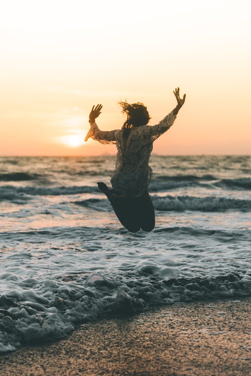 Tourist Jumping Over the Wave Flooding the Beach at Sunset