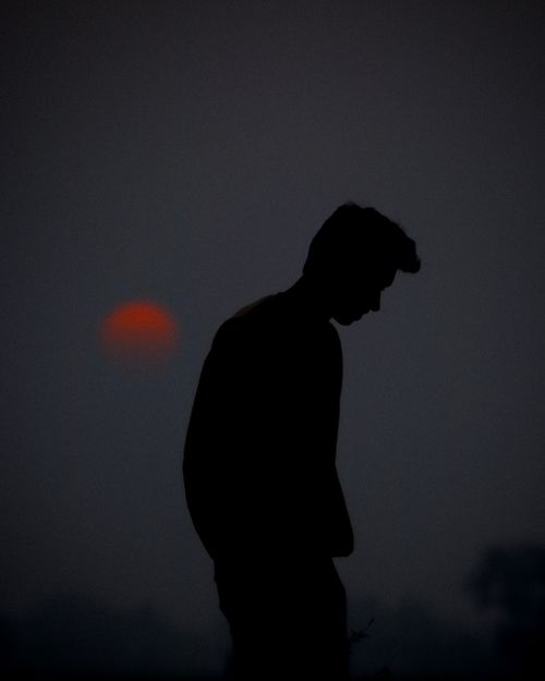 Free A silhouette of a man standing against a dark sunset, creating a dramatic and moody scene. Stock Photo