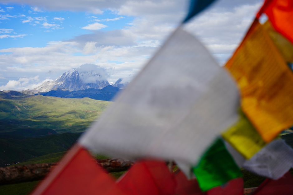 Colorful prayer flags fluttering near majestic mountains under a blue sky.