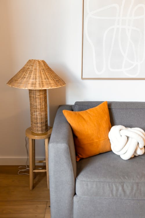 A gray couch with orange pillows and a lamp