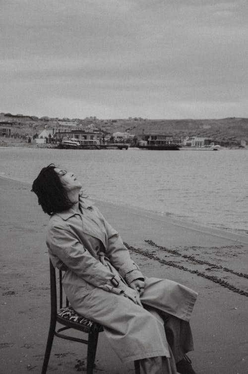 Woman in Trench Coat Sitting on Chair at Beach