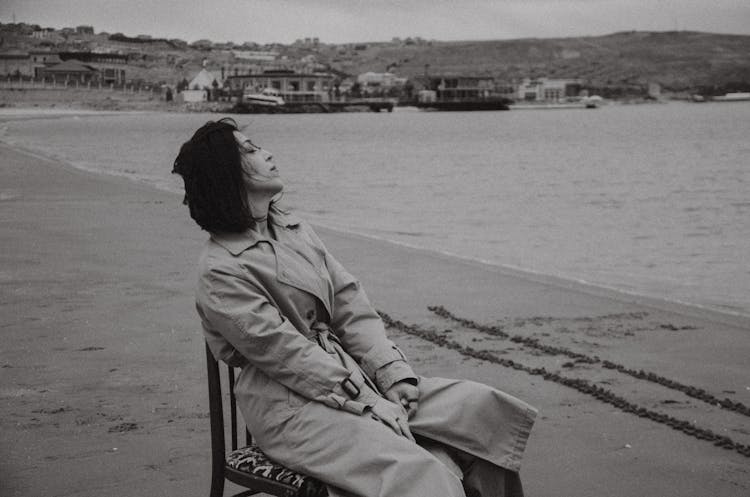 Woman In Trench Sitting On Chair On Beach