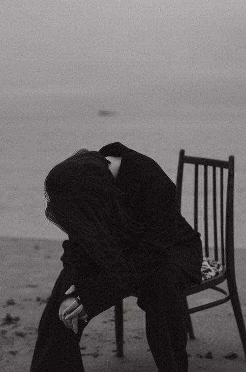 Free Black and white image of a person in black attire, sitting on a chair by the seaside on a foggy day. Stock Photo