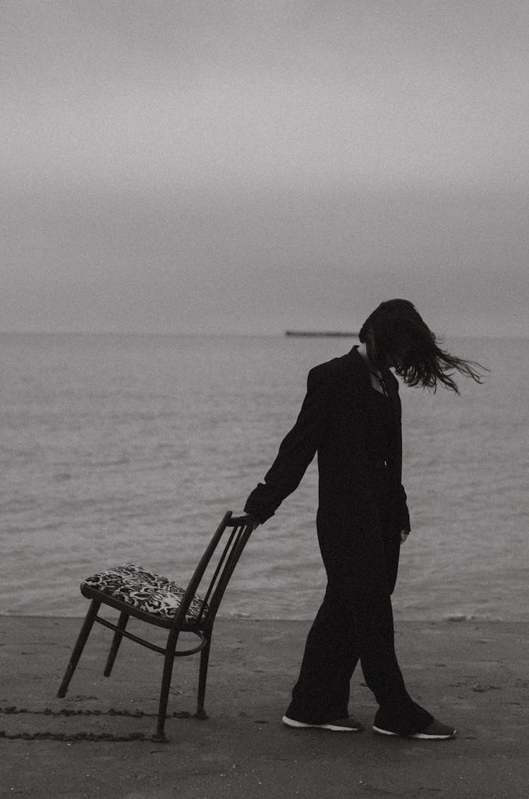 Black And White Shot Of A Woman And A Chair On A Beach 