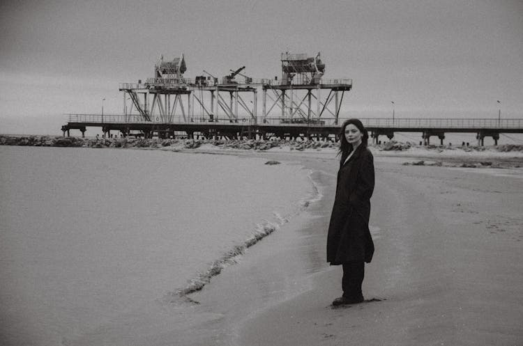 Woman In A Coat Standing On The Beach