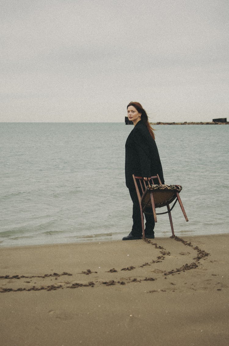 Woman On A Beach Standing And Holding A Chair 