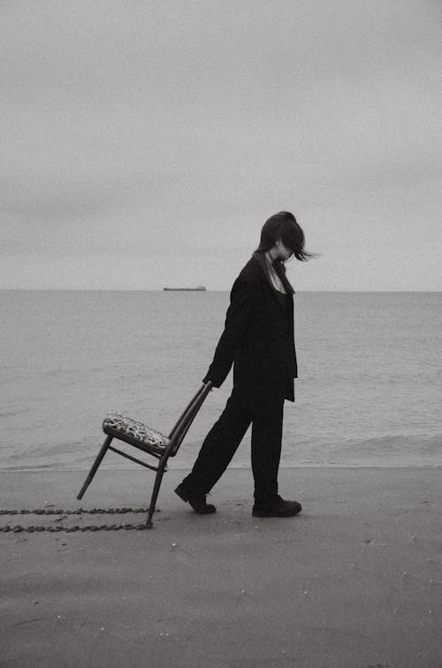 Woman Walking and Dragging a Chair on a Beach 