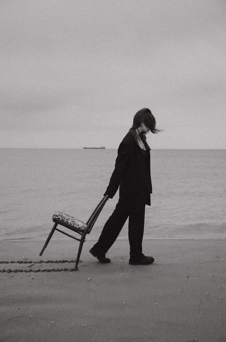 Woman Walking And Dragging A Chair On A Beach 