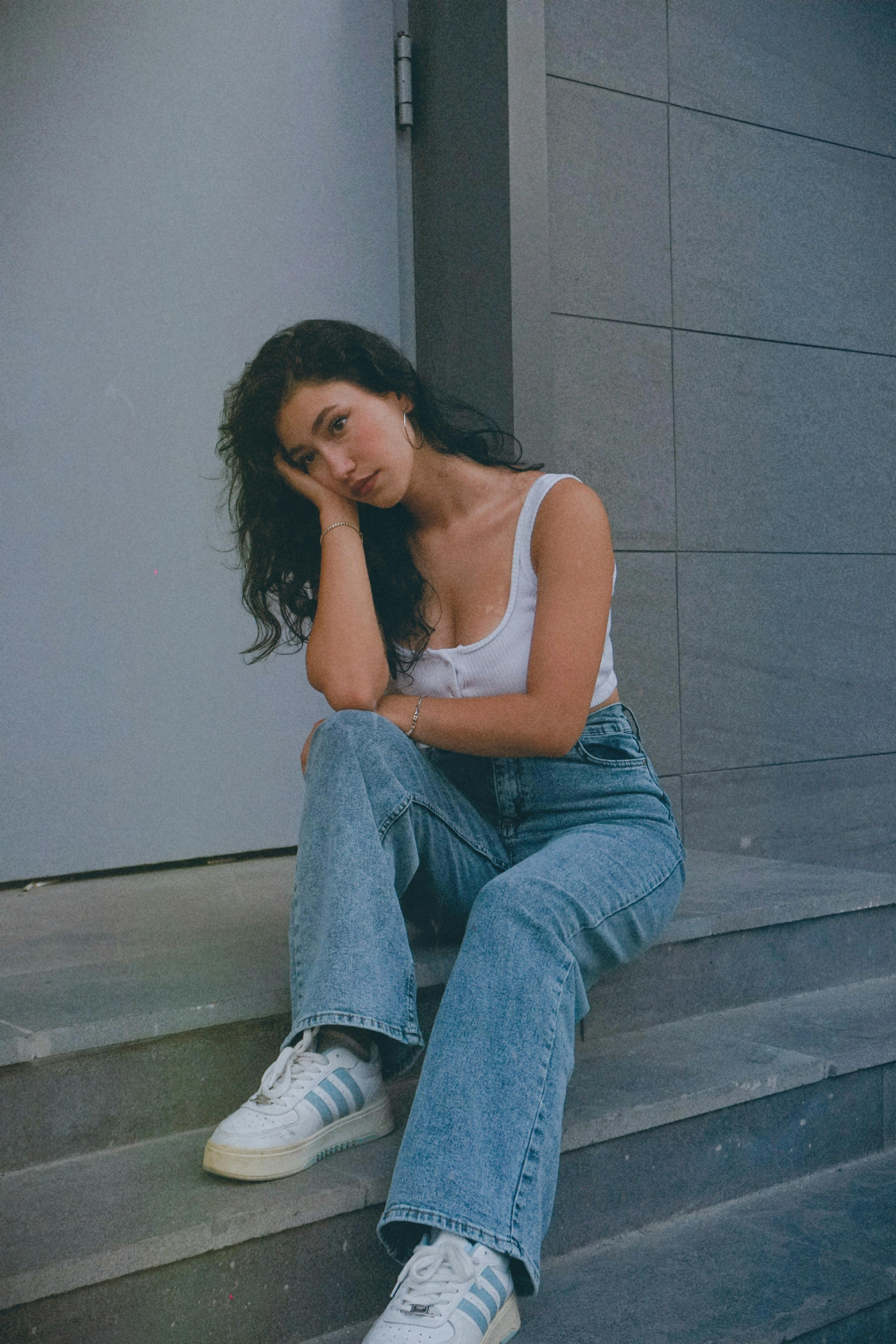 Pensive Model Wearing White Sports Bra and Jeans Sitting on Steps · Free Stock Photo