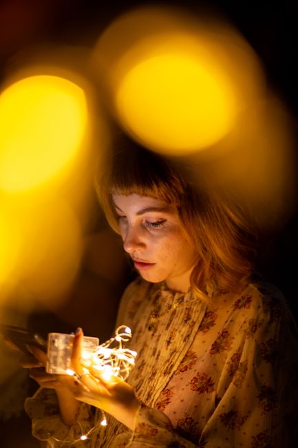 Portrait of a young woman with warm golden string lights, creating a cozy atmosphere.