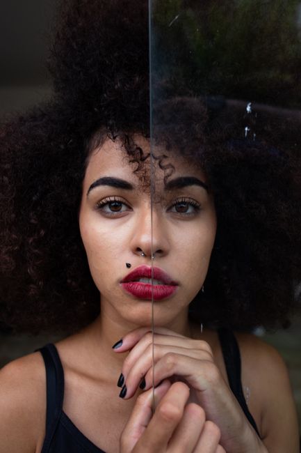 Close-up portrait of a young woman showcasing bold makeup and curly hair through glass reflection.
