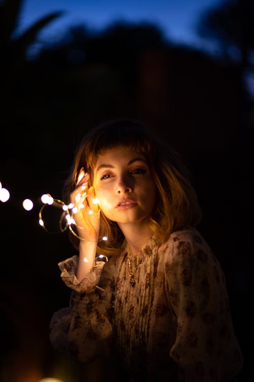 Free Woman in Floral Long-sleeved Top Holding String Lights at Night Stock Photo